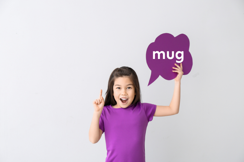 Girl holding a sign that says ‘mug’ and pointing up during a hands-on activity for teaching rhyming words